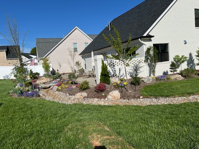 The backyard of a white brick house with colorful flowers and nice landscaping.