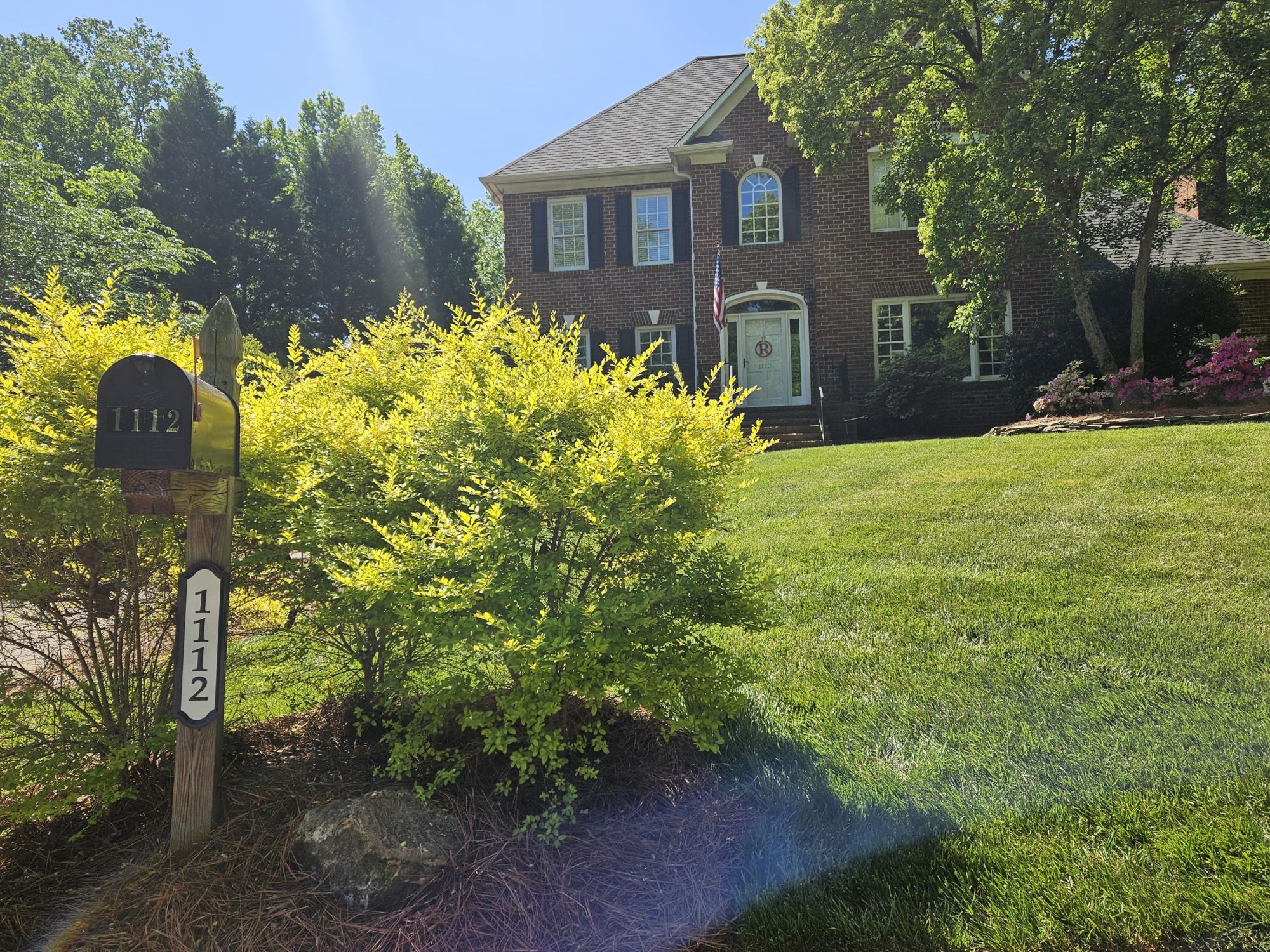 Black mailbox sits by a bush in front of a brick house